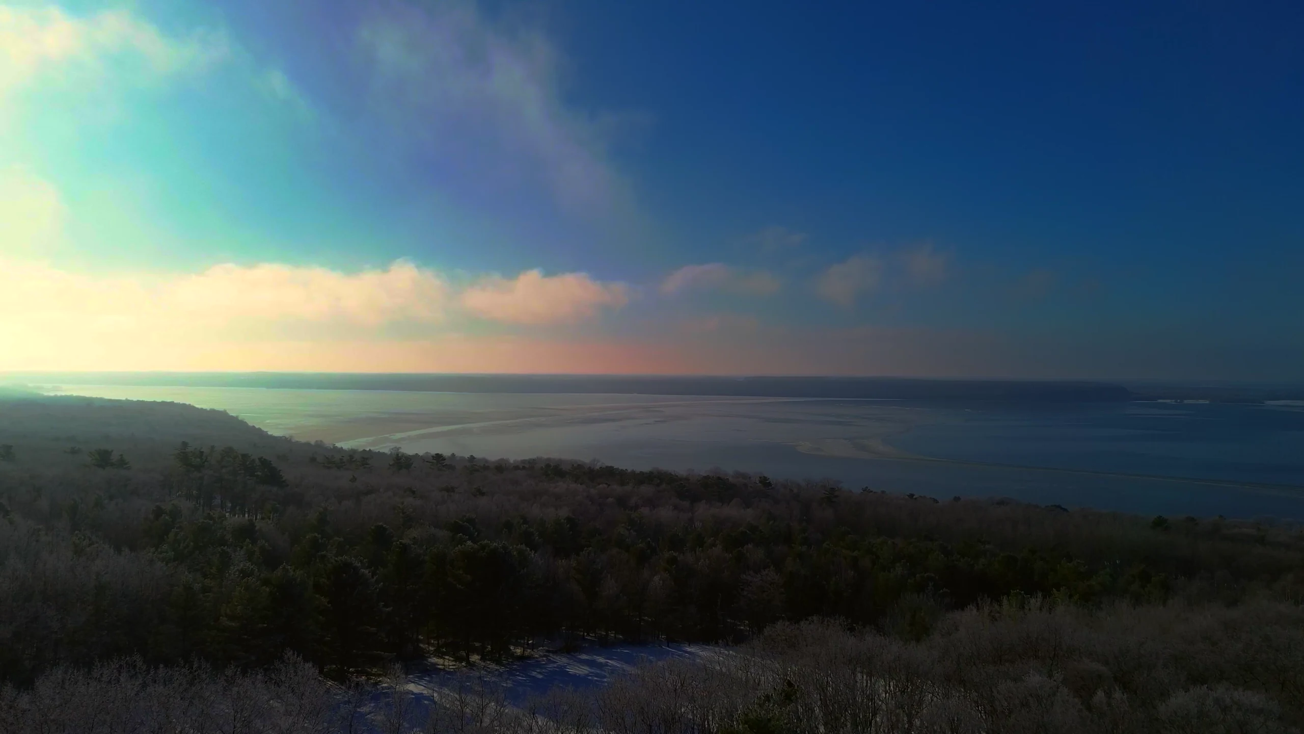 Aerial view across a wooded overlook toward the water at sunrise