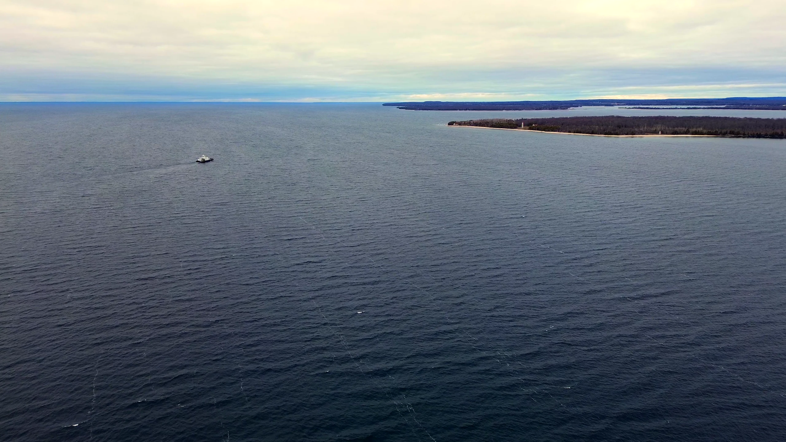 A small boat crossing open water near a distant lighthouse
